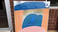 Front view of abstract acrylic painting leaning against wall, showing curved blue shapes contrasting peach background with soft yellow and pink elements.