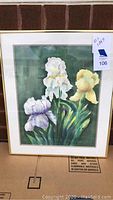 Framed painting showing white and yellow iris flowers with green leaves on a green background, with a gold frame and matting.