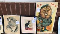 Three framed animal pictures together including the Lion Coffee ad, black cat print, and lemur print.