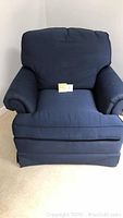 Front view of a navy blue upholstered armchair with cushioned seat and back, rolled arms, and a skirted bottom.