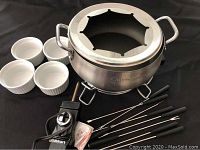 Photo showing Cuisinart stainless steel electric wok with temperature control unit on base, eight black-handled fondue forks, four white ceramic ramekins, and a small clear measuring cup.