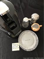 Photo showing four Tiffany & Co. crystal dessert plates stacked, sugar and another glass container with metal lid, beige ceramic milk creamer, and black coffee server.