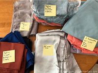 Arrangement of tablecloths, napkins, and table runners labeled with sizes and colors on sticky notes.