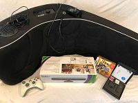 Black Boom gaming chair with AC adapter and audio cables, Xbox 360 controller, Xbox Kinect sensor in box, Guitar Hero game, and two Nintendo DS games with cases.