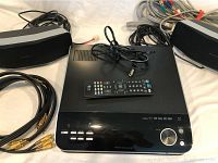 Front view of LG surround sound system receiver, two wireless speakers and remote control with cables.