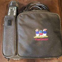 Black carrying case with ViewSonic embroidered logo, attached remote control in nylon holder, and cables partially visible.