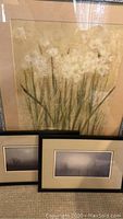 Silver framed print of white paperwhites flowers with green stems on beige background, two smaller black framed landscape prints in front.