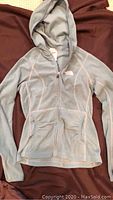 Light gray North Face zip-up hoodie laid flat on a dark surface, showing front view and hood.