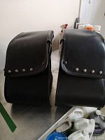 Pair of black leather Honda saddlebags side view showing flap closure with metal studs and smooth leather finish.