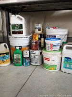 Photo showing a grouping of various renovation product containers including stain, cleaner, and waterproofer in buckets and cans arranged on a floor.