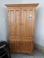 Front view of solid oak entertainment armoire showing bifold upper doors and double lower doors with wood grain and knobs.