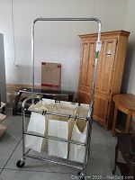 Front view of chrome metal hamper station with 3 cream polyester bags hanging for laundry sorting on caster wheels.