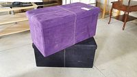 Two storage ottomans stacked, purple ottoman on top of black ottoman, showing rectangular shape and ultrasuede upholstery.