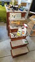 Photo showing wooden pet stairs with carpeted steps, decorative dog-themed signs attached to stair risers, dog harnesses, pet clipper, rope toy, and grooming bottles arranged on the steps.