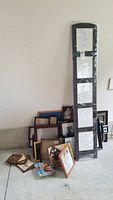 Wide view showing stacked assorted picture frames and a tall five-panel floor-standing picture frame wrapped in plastic leaning against the wall.