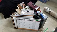 Photo showing file totes, paper shredder, whiteboard calendar, and various office supplies piled together.