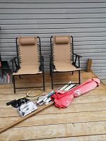Two tan fabric metal folding chairs with black frames, a rolled up red Budweiser patio umbrella, automotive parts including wiper blades and horns on wooden decking.
