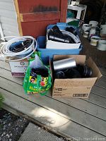 Four boxes and a green reusable shopping bag filled with assorted PVC pipe fittings, hoses, and tubing in various sizes and materials.