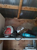Black and Decker circular saw, saw blades, and Makita electric drill together on shelf