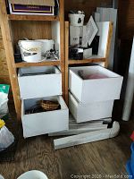 Two wooden shelving units with four white drawers on casters filled with various hardware items including vents, baskets, and pipes.