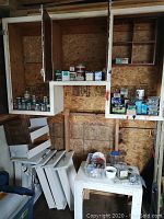 Three wooden cupboards open showing assorted hardware boxes and small wood table beneath
