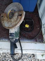 Electric cement saw showing top of rusted blade, green and black body, and yellow power plug.
