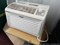 Full side view of Haier window air conditioner placed on a wooden board showing front grill, control knob and power cord.