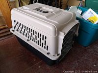 Side view of beige and black plastic pet carrier with multiple ventilation slots and handle on top