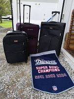 Photo showing three carry-on luggage bags (Air Canada black, Outbound purple, Boarding Blue black) and Patriots Super Bowl Champions banner laid in front.