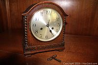 Front view of tiger oak mantel clock on wood surface with winding key at base
