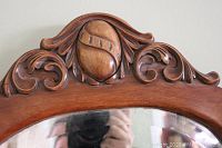 Close-up of the carved ornate crest at the top of the oak mirror frame showing decorative scrollwork and central oval carved element.