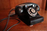Front angled view of the black rotary dial telephone showing the body, dial, and handset with cord extending from the handset.
