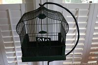 Front view of green vintage birdcage on curved wrought iron stand showing cage structure and shape
