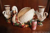 Photo shows the large swan centerpiece with colorful Christmas-themed base and two swan vases on either side with a soda can for scale on a wooden surface.
