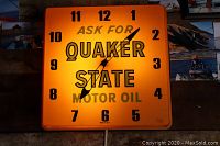 Square illuminated wall clock with Quaker State Motor Oil logo on orange background