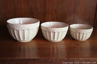 Three white glazed mixing bowls with embossed floral design on wood surface