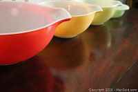 Side view of four graduated sized Pyrex mixing bowls lined up, showing colors red, yellow, lime, and green with pour spouts.