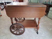 Side view of tea wagon with one drop leaf extended, showing wheels and lower shelf.