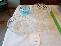 Four items on table: two clear crystal vegetable bowls, one clear crystal candy dish, and one blue glass candle holder. All items shown from a top-side view.