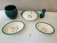 Three serving dishes and two pieces of green glazed pottery on a white tablecloth.