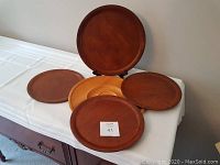 All five round wooden trays displayed on a white cloth-covered surface showing different warm brown wood tones and sizes.