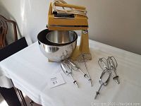 Yellow GE stand mixer with two stainless steel bowls on table, showing attachments spread out