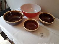 Four mixing bowls on white tablecloth: one large red bowl and three brown bowls of varying sizes.