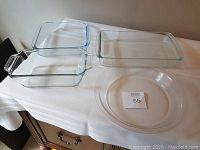 Four clear glass Pyrex baking dishes on white cloth, two rectangular with handles, one square, and one round dish.