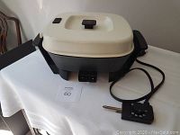 Electric frying pan with cream lid and black base, showing cord and temperature control dial on side.