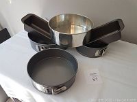 Two rectangular loaf pans stacked on top of a large springform pan and a stainless steel round cake pan on a white tablecloth.