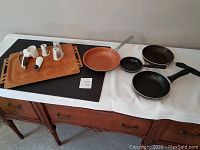 Full view of four frying pans and a box grater on wooden tray on furniture
