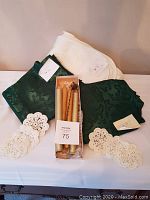Photo showing white padded table cover, green patterned runner, six white crocheted doilies, and box of four decorative candles.