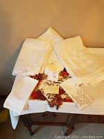 Photo showing the folded tablecloths, napkins, and runner arranged on a wooden table with a beige background.