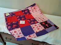 Full view of the handmade quilt spread on a wooden dresser, showing patchwork design with red, purple, and pink blocks, some with red hats and floral prints.